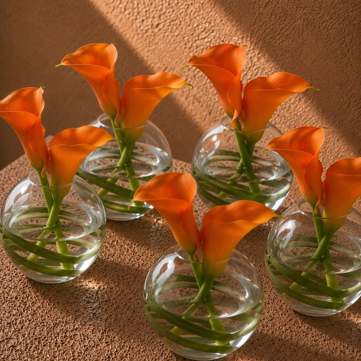 Stella orange calla lily arrangements with bear grass in small round clear glass vases by AIWA Flowers