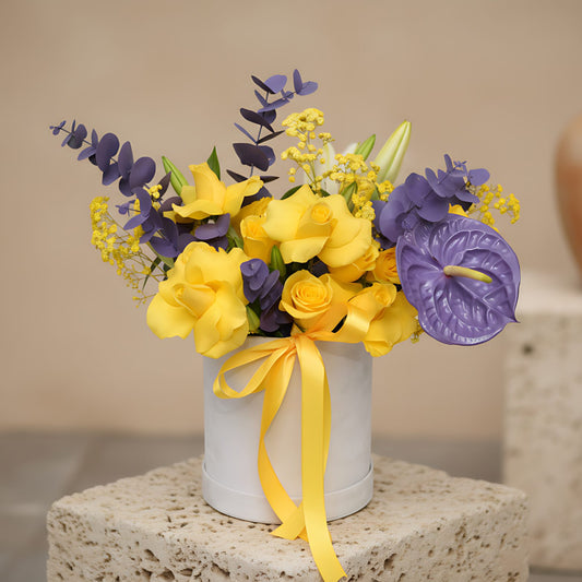Tease floral arrangement with yellow roses, white lilies, purple anthurium and eucalyptus in a white velvet box by Aiwa Flowers