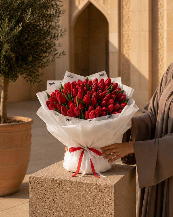 Woman in abaya holding a lush red tulip bouquet in white wrap with red ribbon - Tulip Wonderland by AIWA Flowers