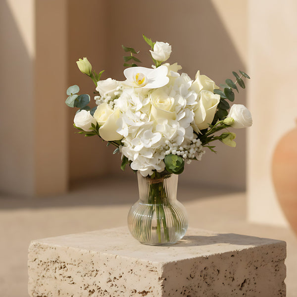 Vanessa arrangement with white roses, white hydrangea, orchid and eucalyptus in a clear glass vase