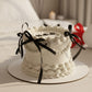 close up of vanilla birthday cake with cream decoration and black ribbons on elegant setup