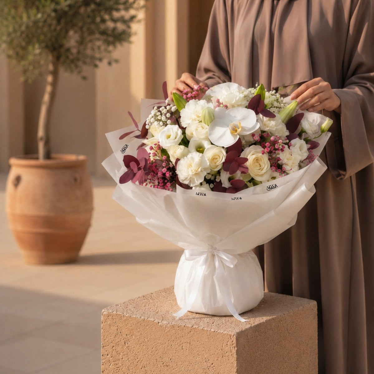 Woman holding a white rose, orchid & lisianthus bouquet in white wrap - Velour Sky by AIWA Flowers
