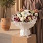 Woman holding a white rose, orchid & lisianthus bouquet in white wrap - Velour Sky by AIWA Flowers