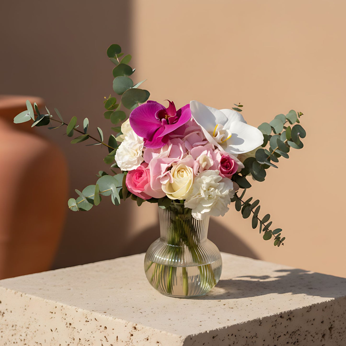 Violet arrangement with white and pink roses, orchids, hydrangea and eucalyptus in a clear glass vase