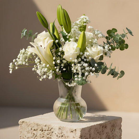 Waltz arrangement with white roses, lilies, gypsophila and eucalyptus in a clear glass vase