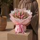 Woman holding a lush pink tulip bouquet in blush wrap with pink ribbon - Whispering Tulips by AIWA Flowers