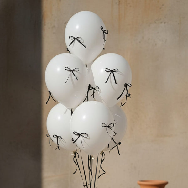 White helium balloon bouquet decorated with black ribbon bows in a minimal luxury arrangement
