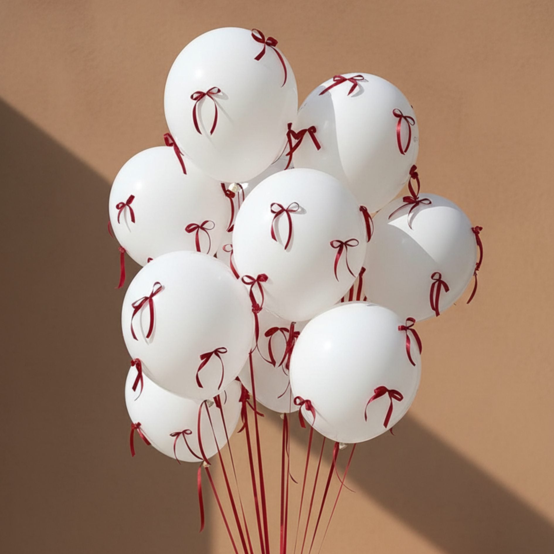 Close-up of white helium balloons decorated with red ribbon bows in a minimal luxury style